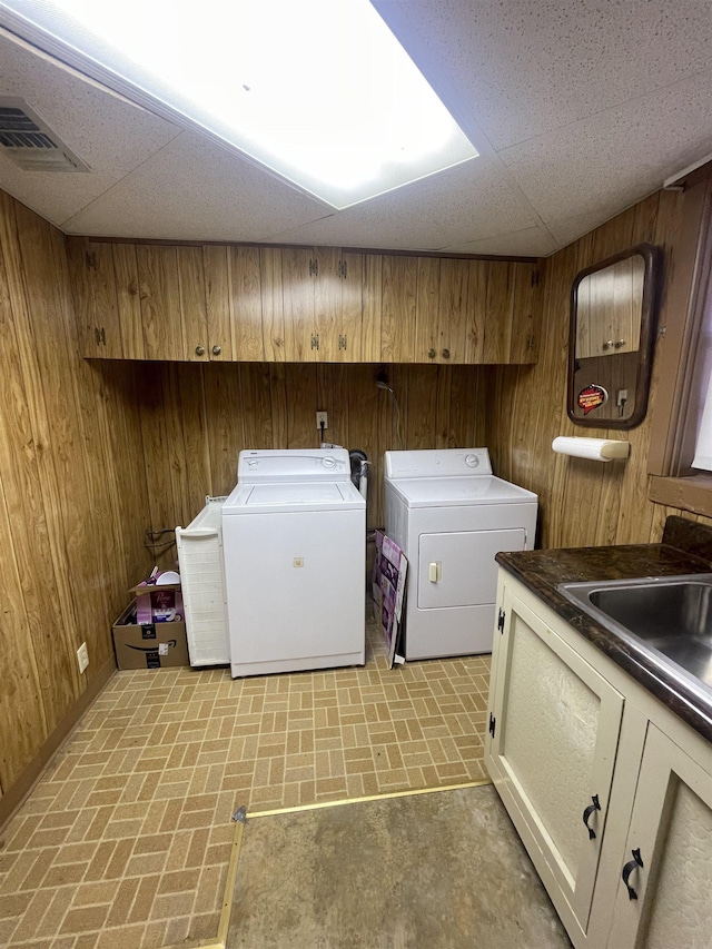 laundry room with washing machine and clothes dryer, wooden walls, sink, and cabinets