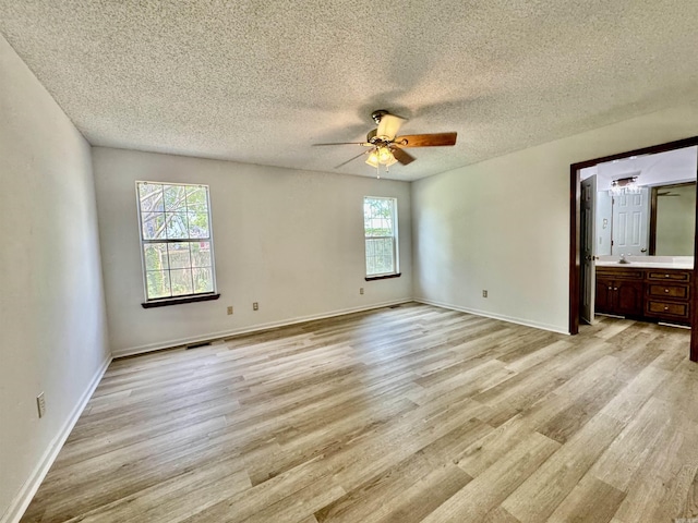 unfurnished bedroom with ceiling fan, a textured ceiling, connected bathroom, and light hardwood / wood-style flooring