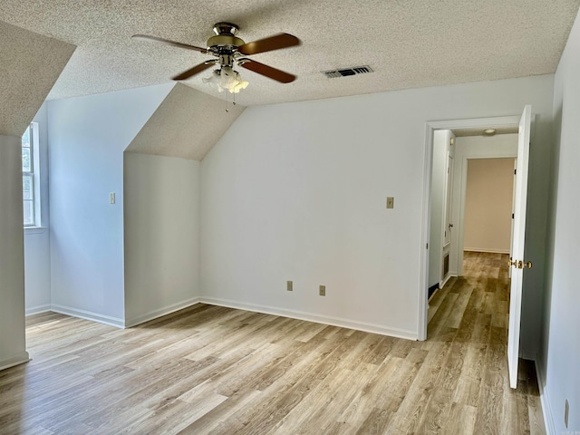 additional living space featuring a textured ceiling, ceiling fan, light hardwood / wood-style flooring, and vaulted ceiling