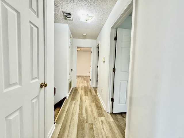 hallway with light hardwood / wood-style flooring and a textured ceiling