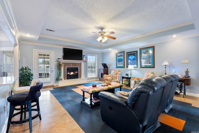 living room with a textured ceiling, ceiling fan, crown molding, and a tray ceiling