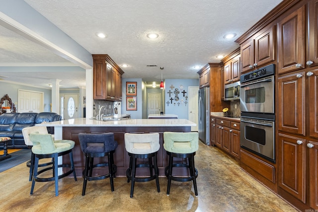 kitchen with pendant lighting, sink, a textured ceiling, appliances with stainless steel finishes, and a breakfast bar area