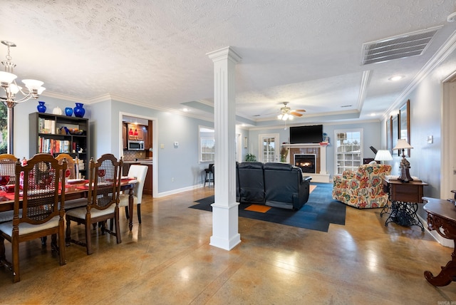 dining area with a tiled fireplace, a textured ceiling, a tray ceiling, and decorative columns