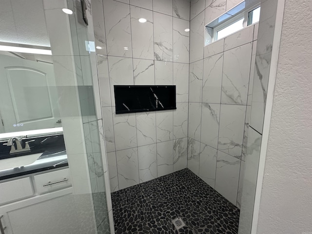 bathroom with tiled shower and vanity