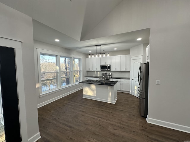 kitchen featuring stainless steel appliances, vaulted ceiling, decorative light fixtures, a center island with sink, and white cabinets