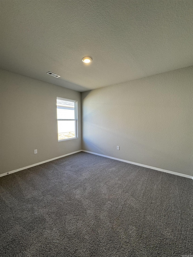 unfurnished room with dark colored carpet, visible vents, baseboards, and a textured ceiling