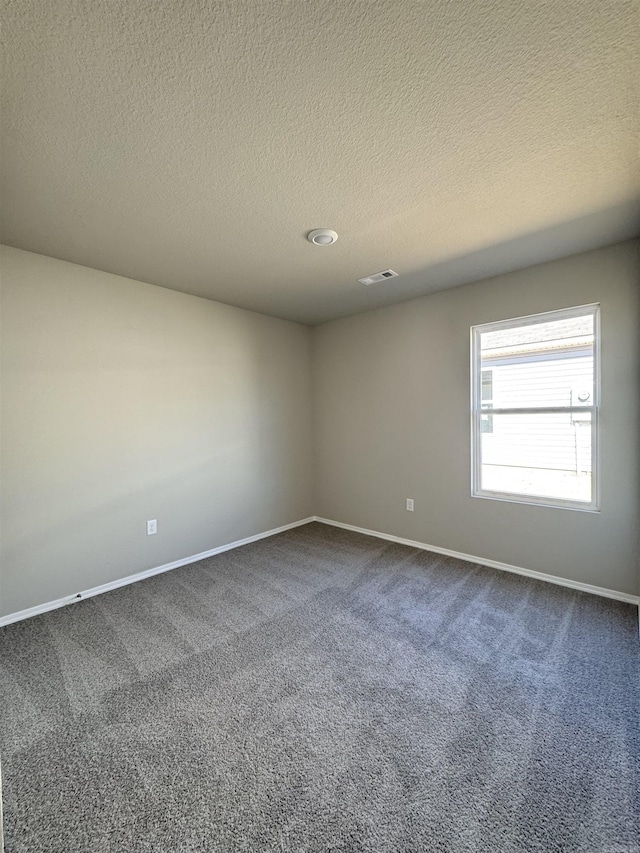 empty room with baseboards, visible vents, dark carpet, and a textured ceiling