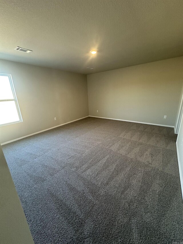 empty room with visible vents, a textured ceiling, baseboards, and dark colored carpet