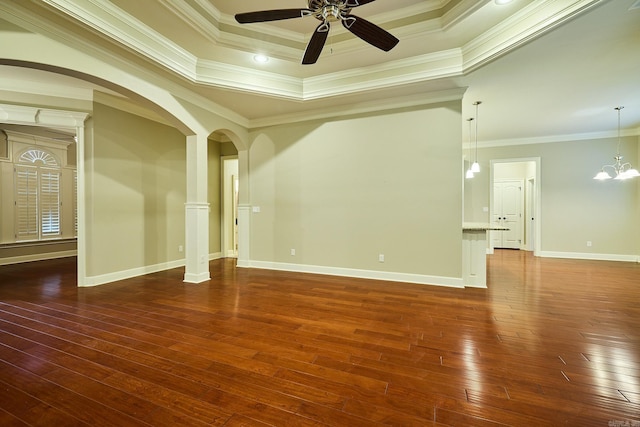 empty room with a raised ceiling, dark hardwood / wood-style floors, ceiling fan with notable chandelier, and ornamental molding