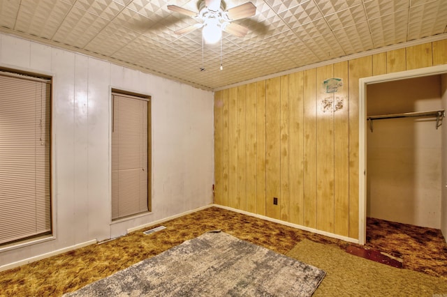 unfurnished bedroom featuring carpet flooring, ceiling fan, wooden walls, and multiple closets