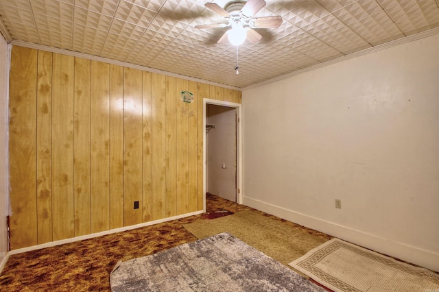 carpeted empty room featuring ceiling fan, wood walls, and ornamental molding