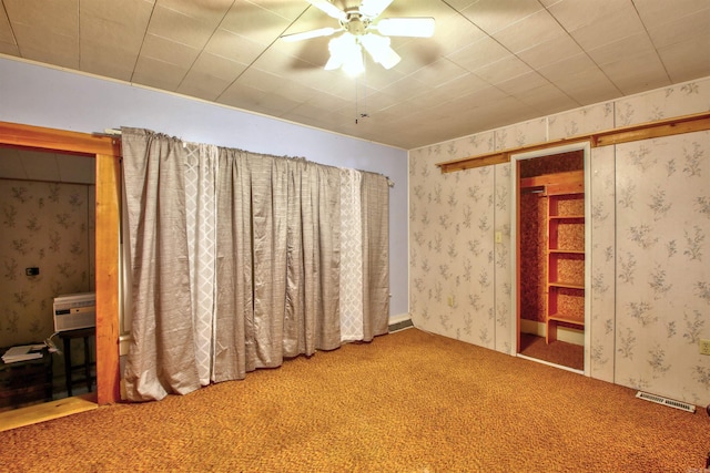 unfurnished bedroom featuring ceiling fan, carpet, and a wall mounted air conditioner