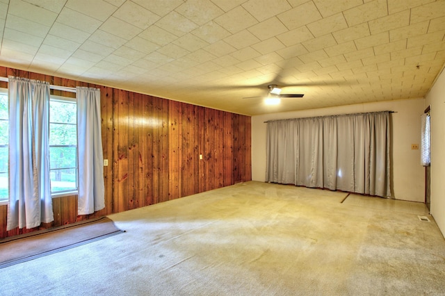 carpeted spare room featuring ceiling fan and wooden walls