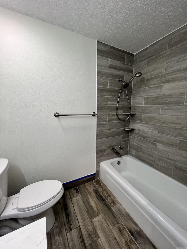 bathroom featuring a textured ceiling, tiled shower / bath combo, and toilet