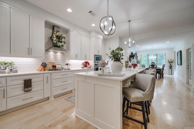 kitchen with white cabinets, appliances with stainless steel finishes, a kitchen island, and wall chimney exhaust hood