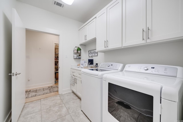 laundry area with washing machine and dryer, light tile patterned floors, and cabinets