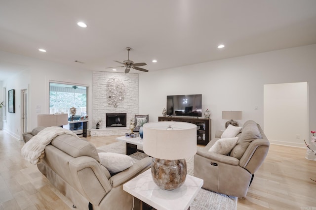 living room featuring ceiling fan, a stone fireplace, and light wood-type flooring