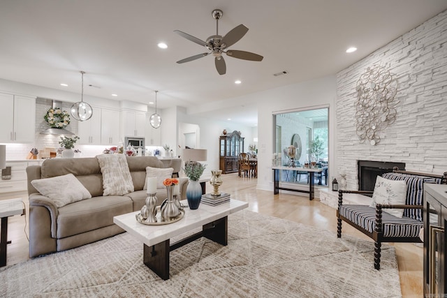 living room featuring light wood-type flooring, a stone fireplace, and ceiling fan