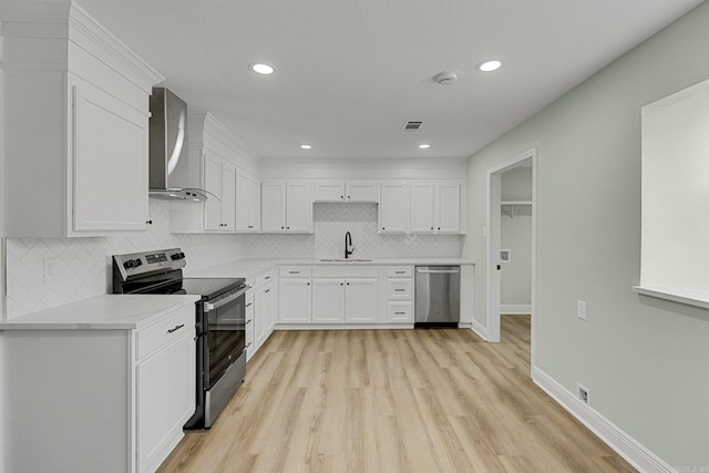 kitchen featuring white cabinetry, sink, wall chimney exhaust hood, light hardwood / wood-style flooring, and appliances with stainless steel finishes