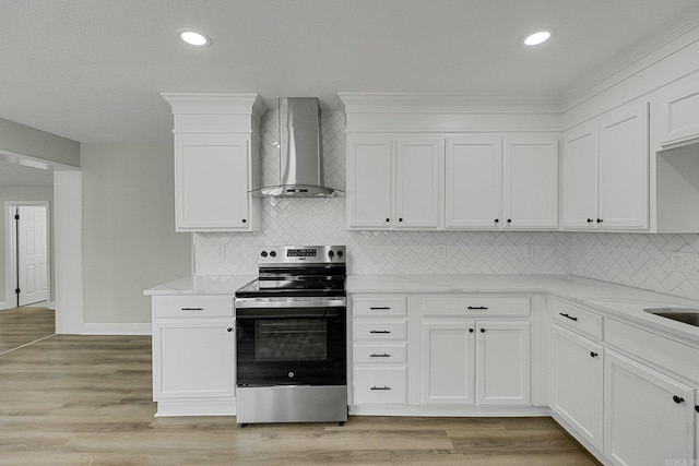 kitchen with stainless steel electric stove, white cabinets, light hardwood / wood-style floors, and wall chimney range hood