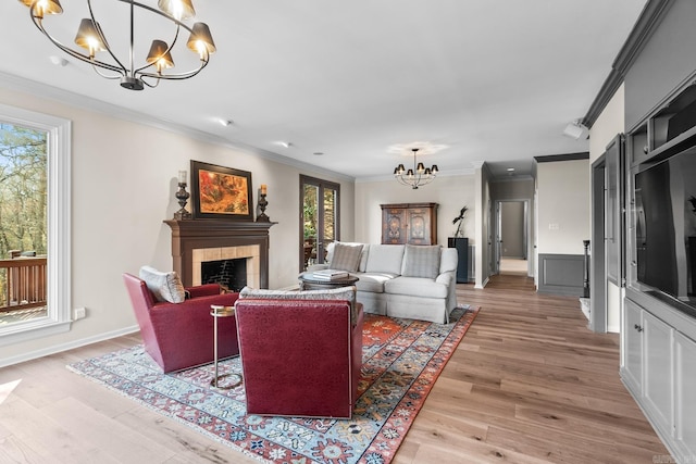 living room featuring a tile fireplace, crown molding, light hardwood / wood-style flooring, and a notable chandelier