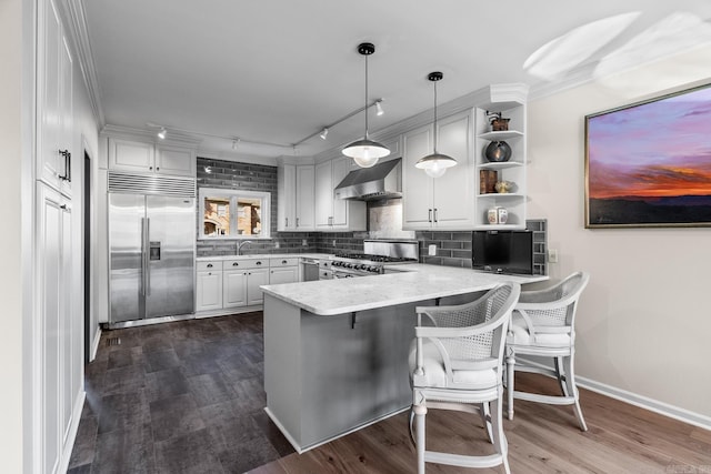 kitchen featuring kitchen peninsula, a kitchen bar, wall chimney exhaust hood, premium appliances, and hanging light fixtures