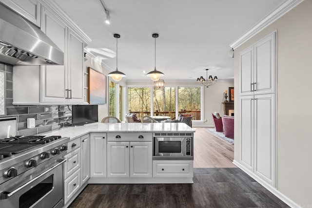 kitchen featuring appliances with stainless steel finishes, ventilation hood, white cabinetry, and decorative light fixtures