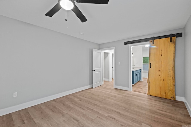 unfurnished bedroom with a barn door, ensuite bathroom, light hardwood / wood-style flooring, and ceiling fan