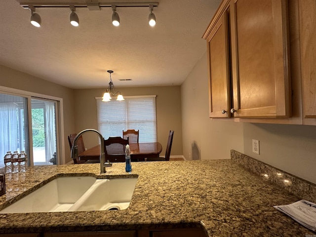 kitchen featuring sink, dark stone countertops, a chandelier, decorative light fixtures, and a textured ceiling