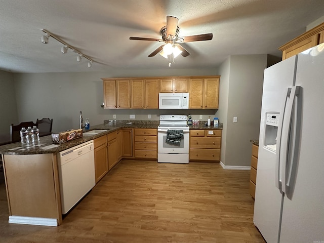 kitchen with sink, kitchen peninsula, dark stone counters, white appliances, and light wood-type flooring