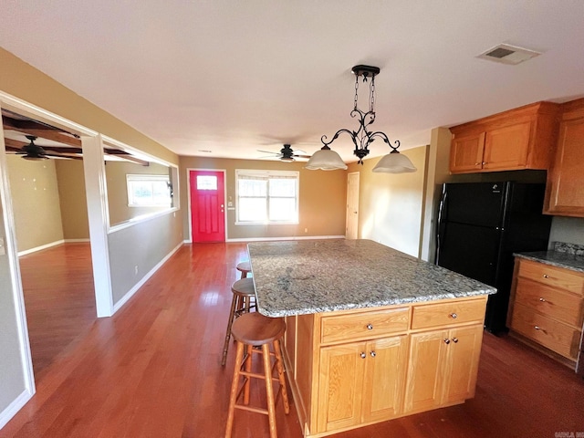 kitchen with a center island, hanging light fixtures, dark wood-type flooring, a kitchen breakfast bar, and black fridge