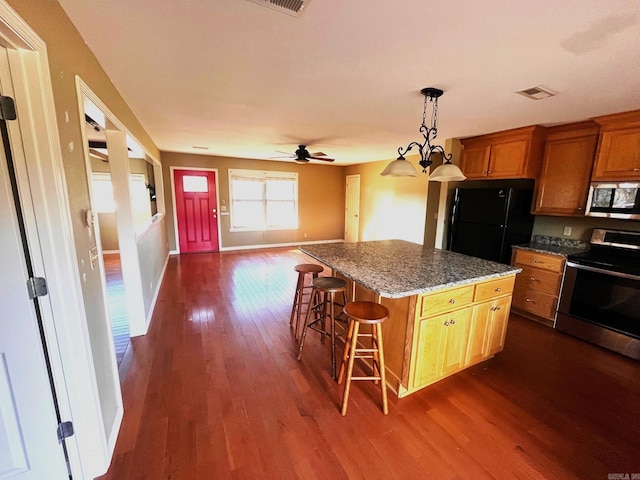 kitchen with dark hardwood / wood-style flooring, a breakfast bar, ceiling fan with notable chandelier, stainless steel appliances, and a kitchen island