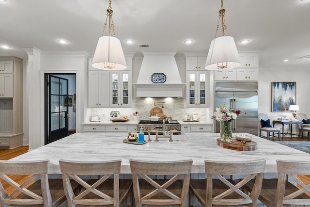 kitchen with a breakfast bar, custom range hood, and built in fridge