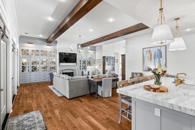 kitchen with hanging light fixtures, light hardwood / wood-style floors, light stone countertops, beam ceiling, and a breakfast bar area