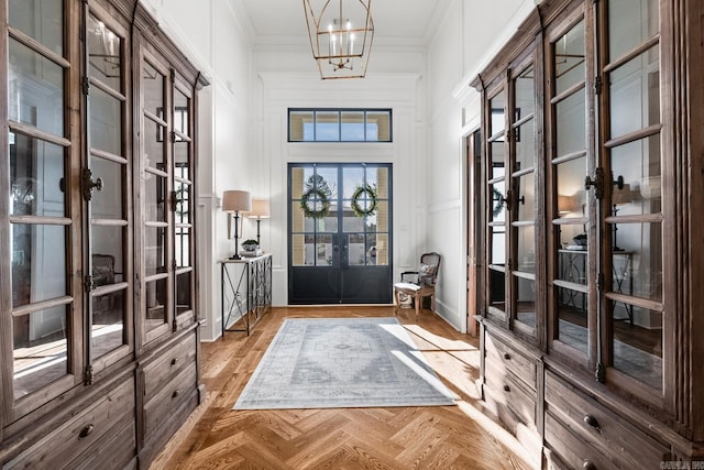 entryway featuring french doors, light parquet floors, ornamental molding, and a notable chandelier