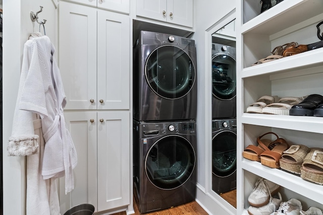 washroom featuring stacked washer / drying machine, light hardwood / wood-style floors, and cabinets