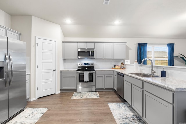 kitchen featuring wood-type flooring, sink, gray cabinets, kitchen peninsula, and stainless steel appliances