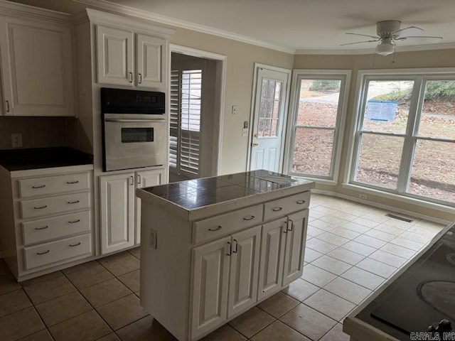 kitchen with wall oven, crown molding, white cabinets, and light tile patterned floors