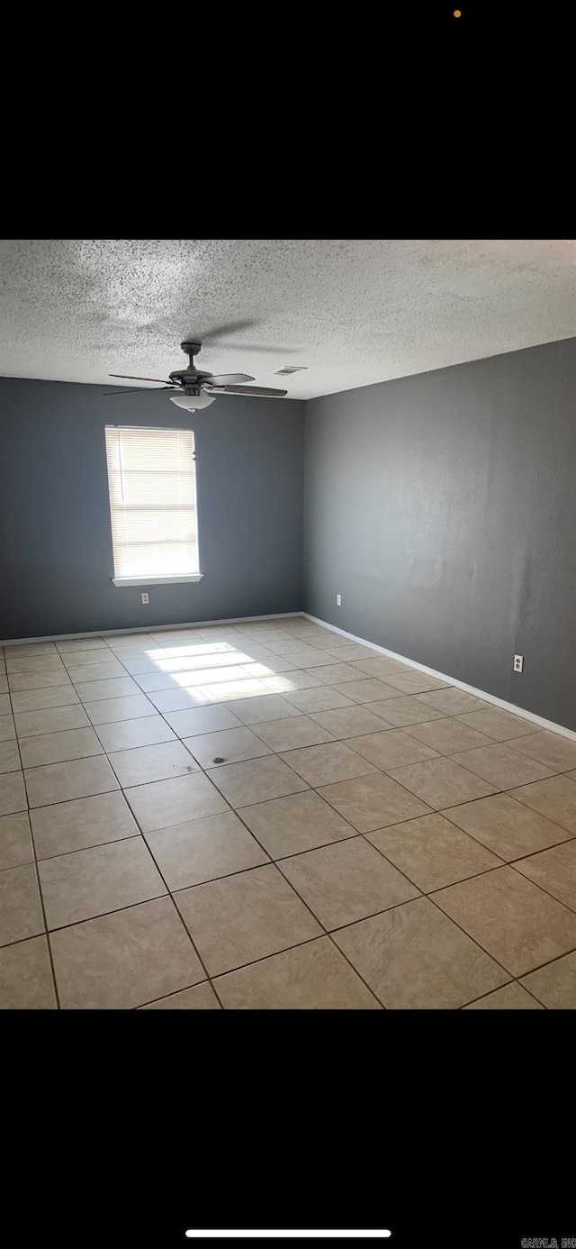 empty room featuring a textured ceiling, ceiling fan, and light tile patterned flooring