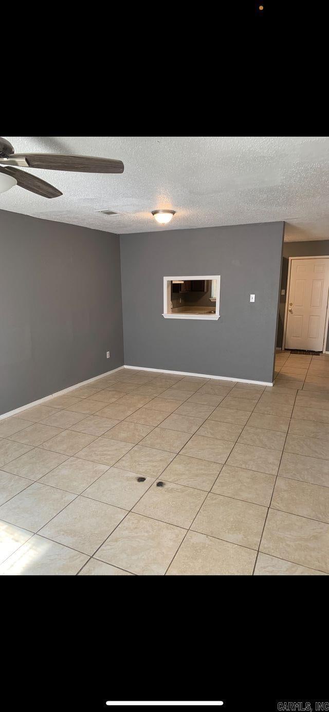 unfurnished room featuring a textured ceiling, ceiling fan, and light tile patterned flooring