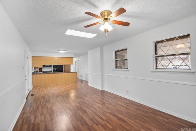 unfurnished living room featuring ceiling fan, dark hardwood / wood-style floors, a textured ceiling, and a skylight