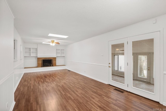 unfurnished living room with a skylight, built in shelves, ceiling fan, a textured ceiling, and wood-type flooring