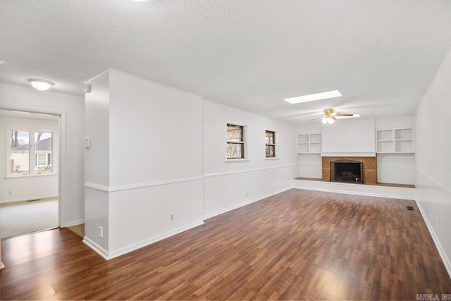 unfurnished living room with a skylight, built in shelves, dark hardwood / wood-style floors, ceiling fan, and a textured ceiling