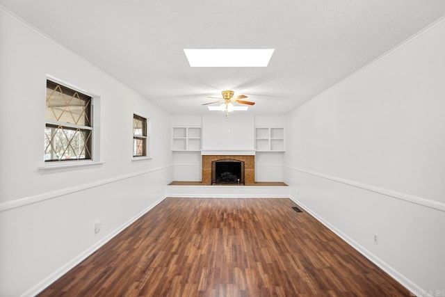 unfurnished living room featuring built in shelves, ceiling fan, a skylight, a fireplace, and hardwood / wood-style flooring