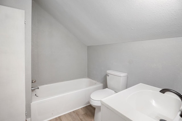 bathroom with vaulted ceiling, a tub, hardwood / wood-style flooring, toilet, and a textured ceiling