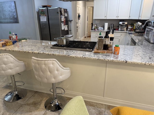 kitchen with light stone countertops, white cabinetry, stainless steel appliances, and a kitchen breakfast bar