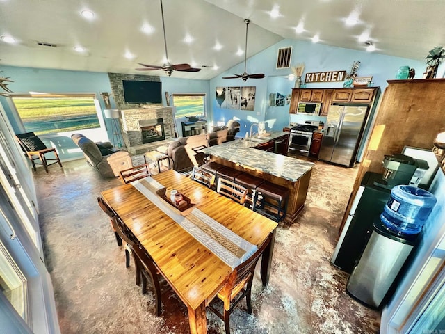 dining area with ceiling fan, a healthy amount of sunlight, a fireplace, and high vaulted ceiling