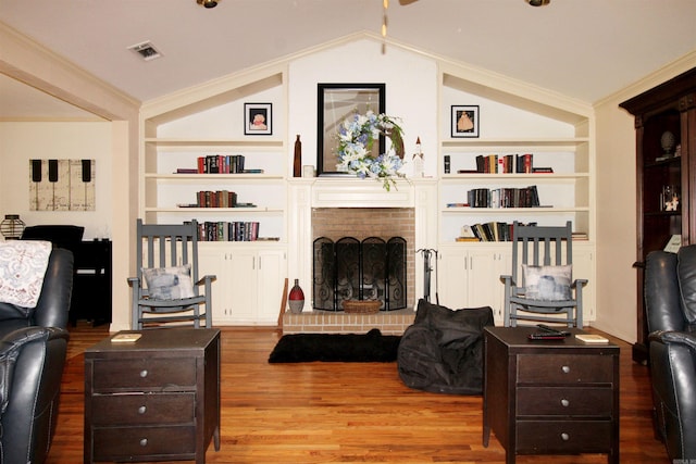 living room featuring ornamental molding, built in shelves, wood-type flooring, a fireplace, and lofted ceiling