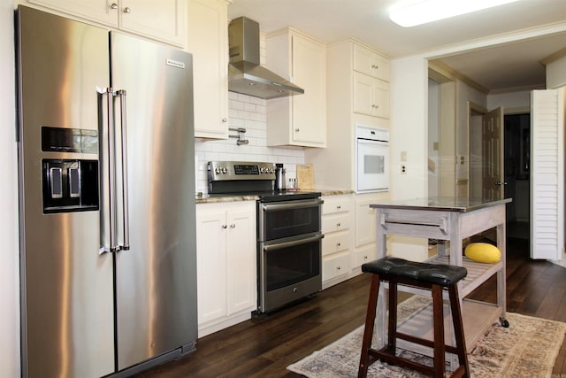 kitchen with decorative backsplash, appliances with stainless steel finishes, light stone counters, wall chimney exhaust hood, and white cabinetry