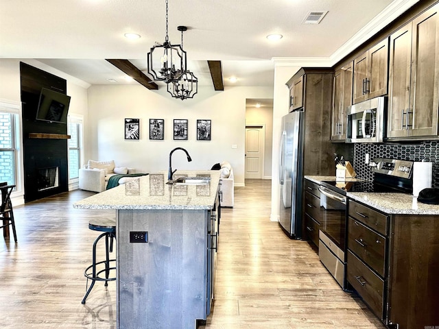 kitchen featuring a center island with sink, sink, light stone countertops, appliances with stainless steel finishes, and beam ceiling